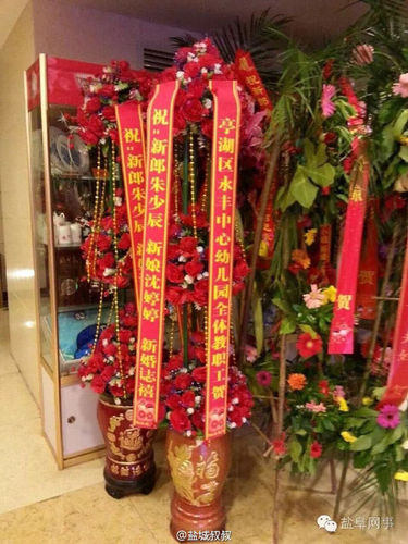 酒店門口擺有不少賓客送來的祝福花籃，其中一個花籃署名為“亭湖區(qū)永豐中心幼兒園全體教職工賀”。