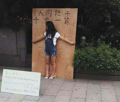 　杭州武林廣場(chǎng)一女孩站在一塊大木板前頭，木板上寫有“人肉靶子，十元一箭”字樣。