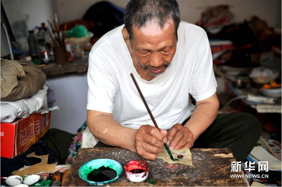6月5日，張奎老人在為雕刻好的皮影上色
