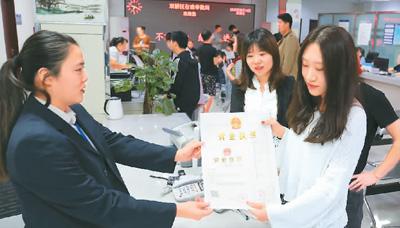 河北省承德市網(wǎng)絡代購經營者陳晨(右)從工作人員手中接過帶有統(tǒng)一社會信用代碼的營業(yè)執(zhí)照。 劉環(huán)宇攝(人民圖片)