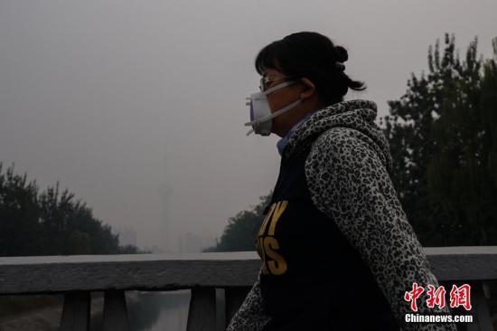 資料圖：北京一名市民戴防霾口罩在戶外行走，遠處的中央電視塔亦被霧霾籠罩。<a target='_blank' href='http://www.chinanews.com/'>中新社</a>記者 崔楠 攝