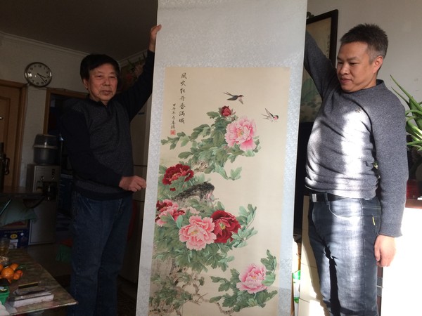 圖為北京工藝美術(shù)大師阮春麟（圖左）與保健中醫(yī)專家王磊在家中展示自己的中國畫作《風(fēng)吹牡丹香滿城》。
